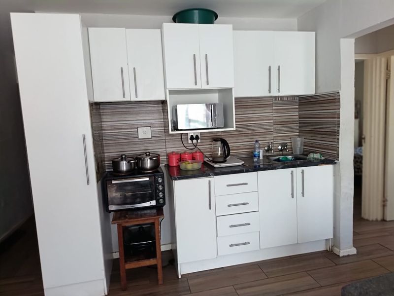 Compact kitchen featuring white cabinetry, a tiled backsplash, laminate countertops, and a stainless steel sink, with wood-look tiled flooring.