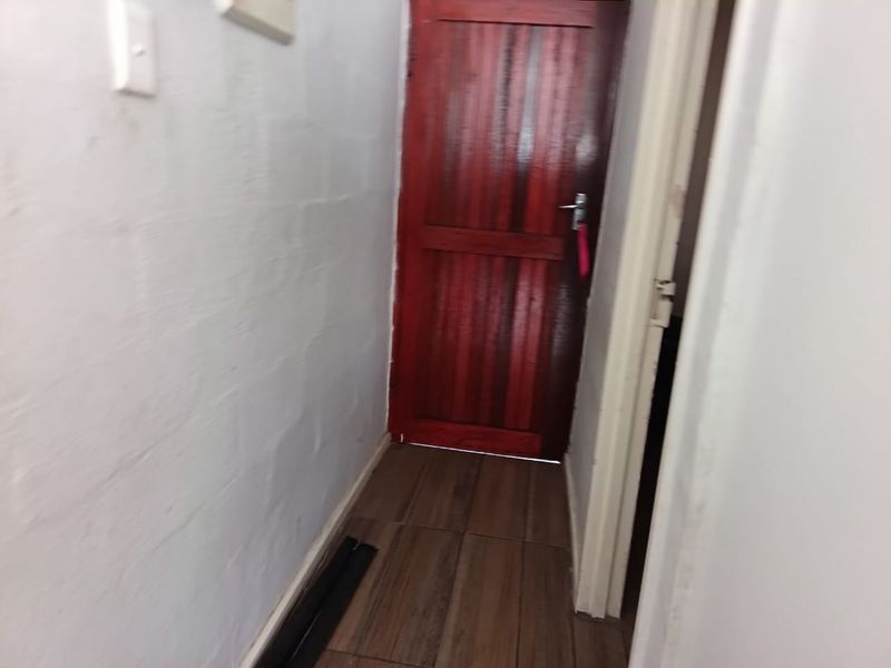 A narrow hallway featuring tiled flooring and a solid wood door, providing access between rooms.