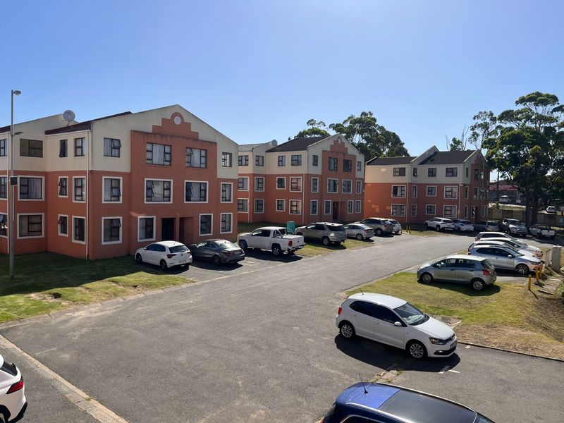Exterior view of a multi-story residential apartment complex featuring an asphalt parking area and established building facades.