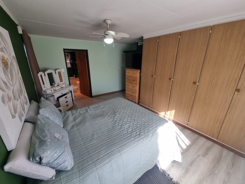 A bedroom featuring built-in wooden cupboards, a ceiling fan, and light-toned laminate flooring, with an adjoining en-suite bathroom.