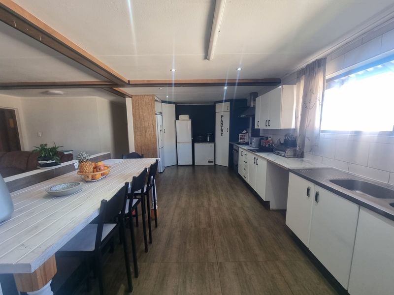 Open plan kitchen and dining area featuring white cabinetry, laminate flooring, and a dedicated pantry cupboard.