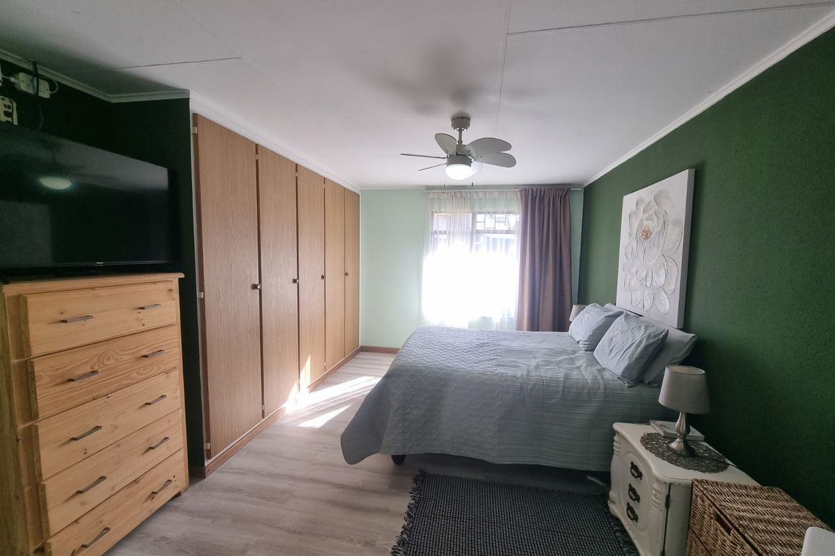 A well-maintained bedroom featuring built-in wooden cupboards, a ceiling fan, and light-toned laminate flooring with a feature wall.