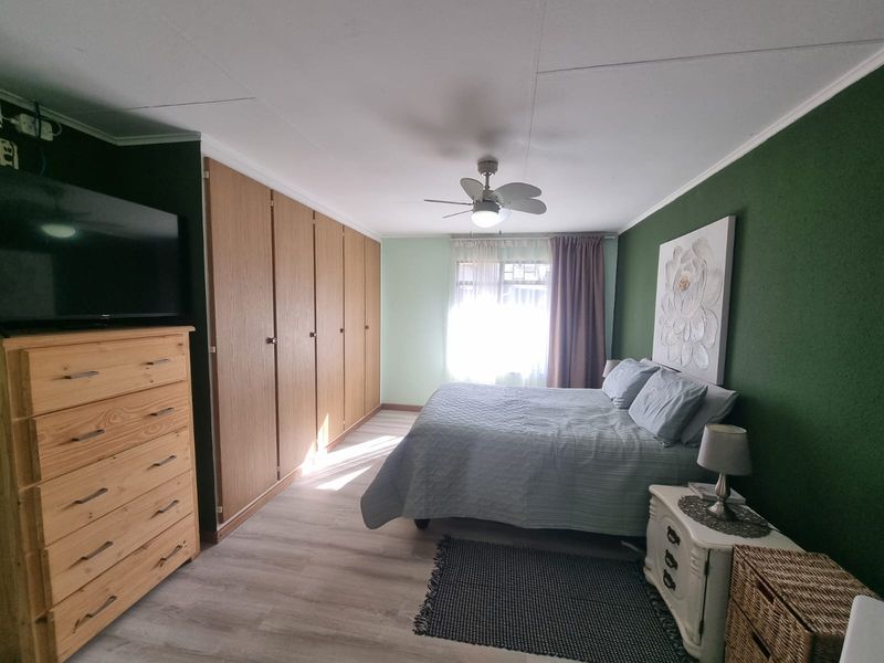 A well-maintained bedroom featuring built-in wooden cupboards, a ceiling fan, and light-toned laminate flooring with a feature wall.