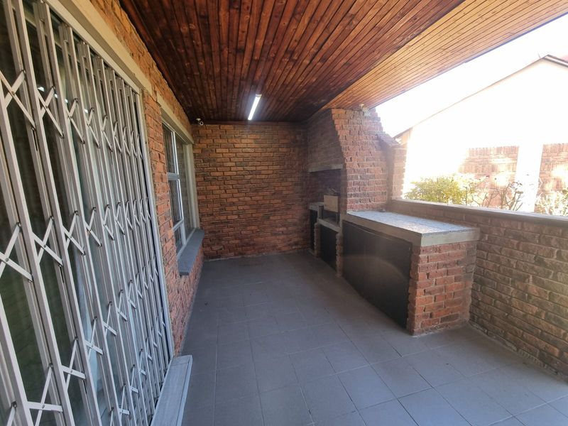 Covered patio area featuring a built-in brick braai, tiled flooring, and a timber-clad ceiling, providing a functional outdoor entertainment space.