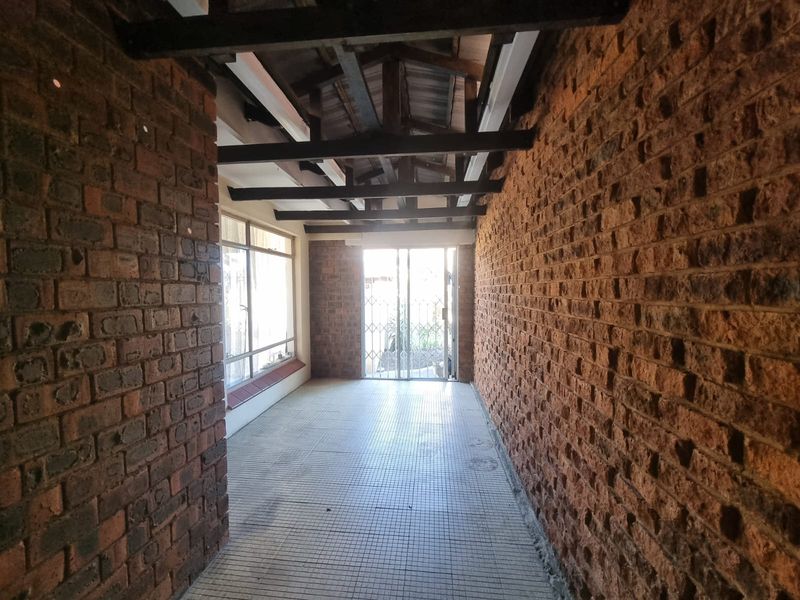 A covered patio area featuring exposed brick walls, timber ceiling beams, and tiled flooring, providing a rustic transition space to the outdoor area.