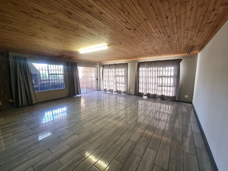 Spacious living area featuring timber tongue and groove ceilings, modern ceramic floor tiles, and large sliding glass doors with security gates.