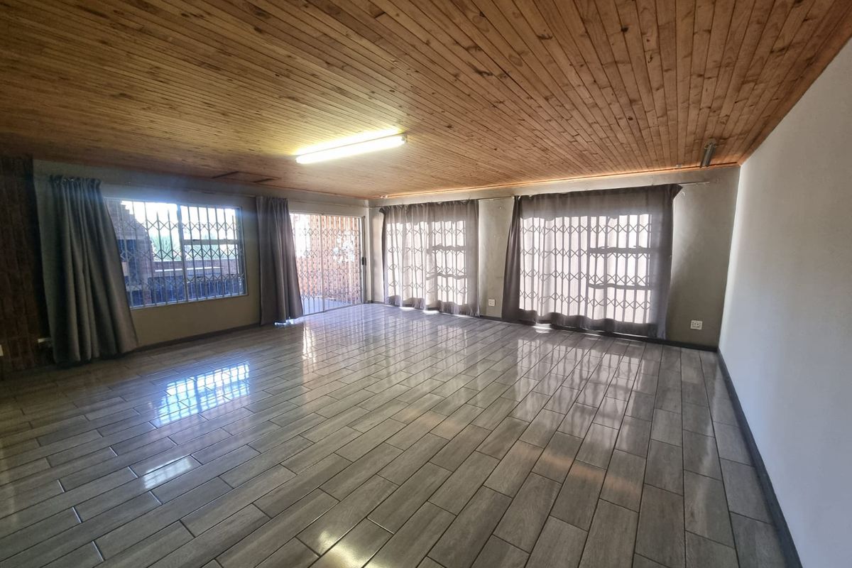 Spacious living area featuring timber tongue and groove ceilings, modern ceramic floor tiles, and large sliding glass doors with security gates.