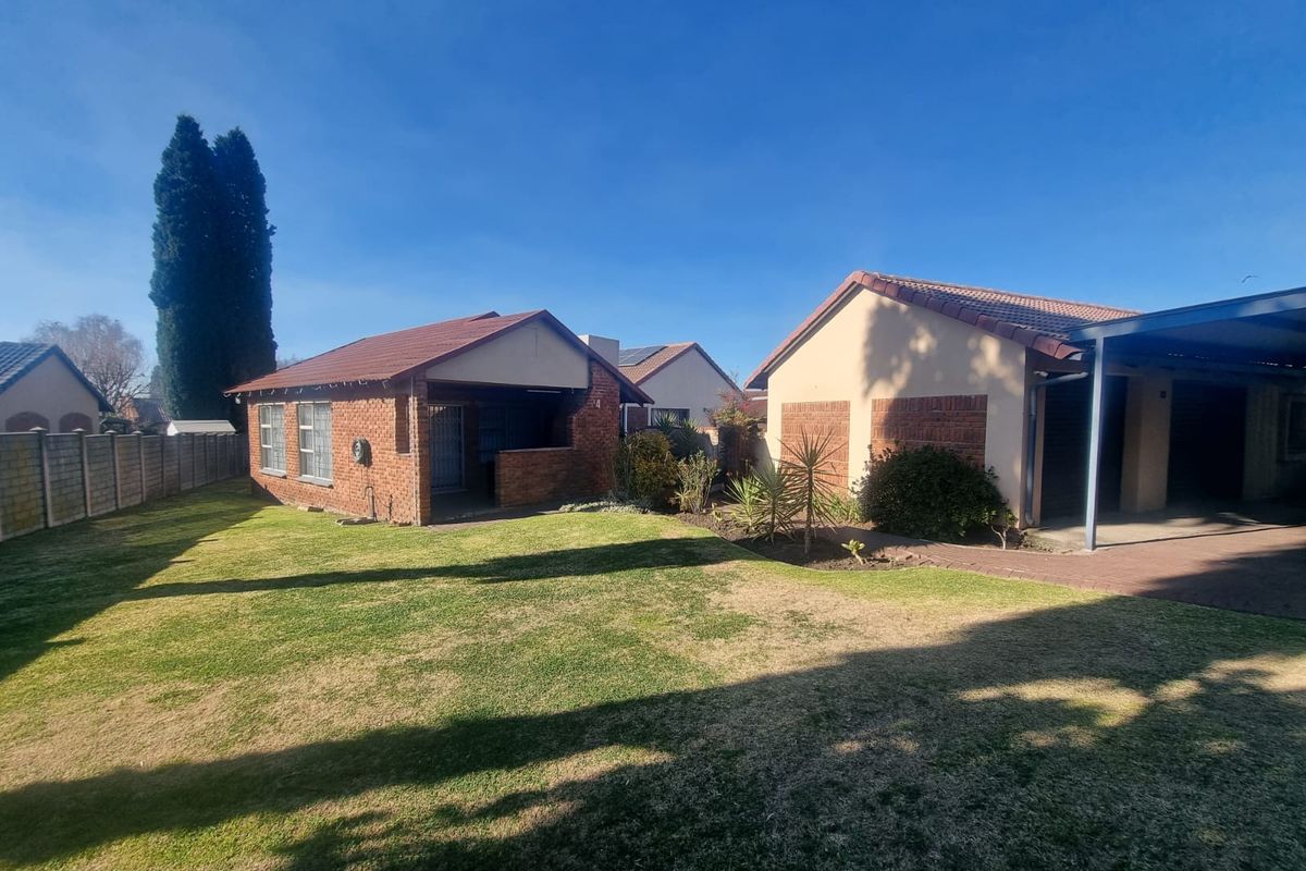 Rear view of the property featuring a brick facade, tiled roof, lawn area, and a paved carport.