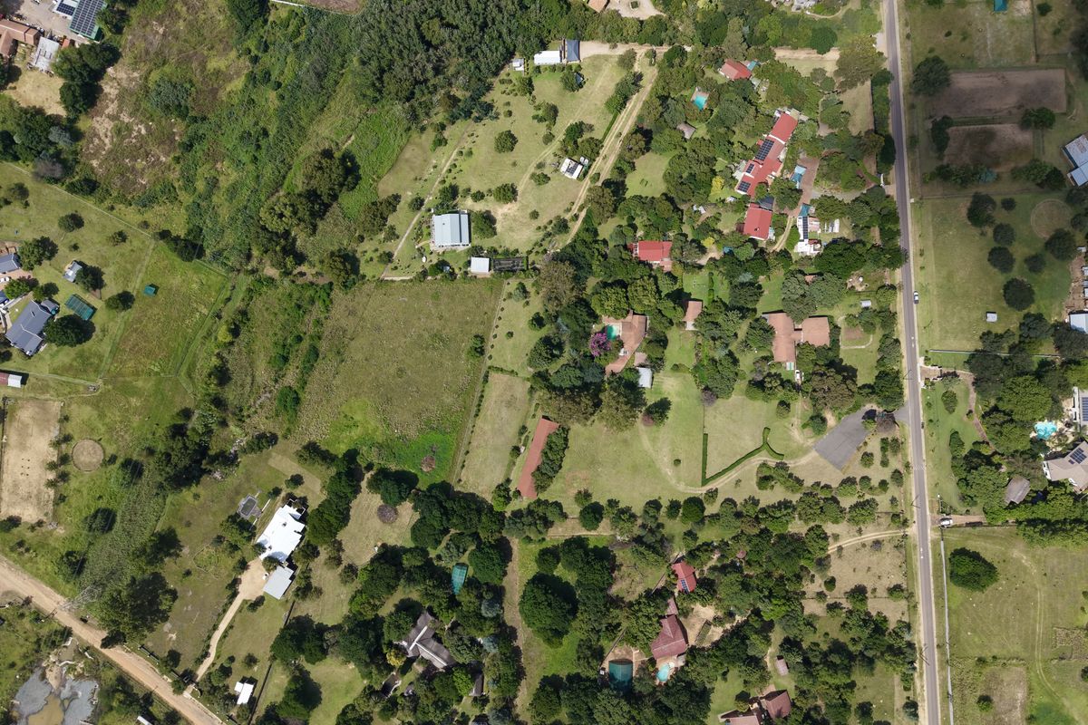 An aerial view of a residential area featuring multiple plots, established trees, and access roads within a semi-rural landscape.