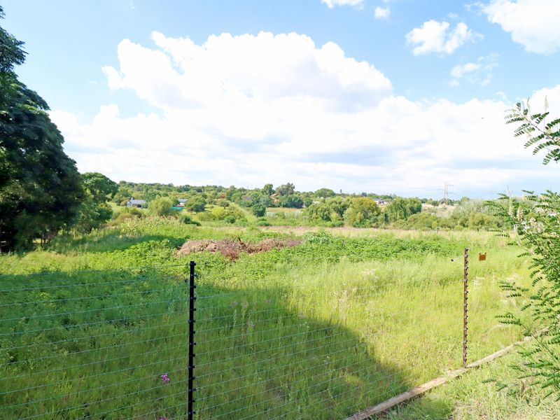 A view of a vacant residential plot featuring natural vegetation and secured by wire mesh and electric fencing.