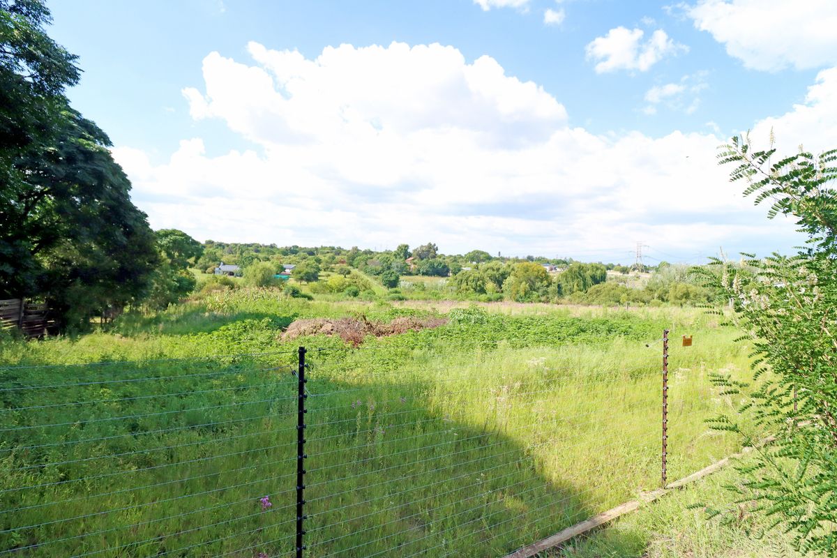 A view of a vacant residential plot featuring natural vegetation and secured by wire mesh and electric fencing.