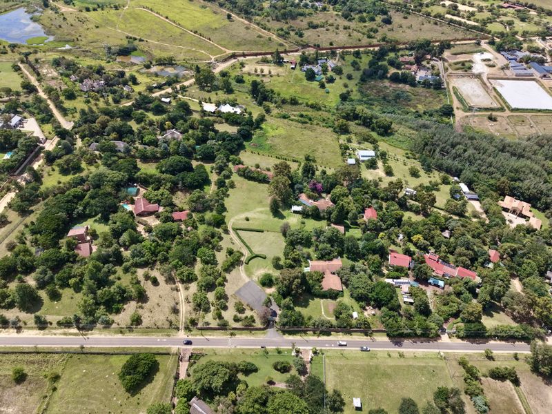 An aerial view of a residential property featuring expansive green grounds, mature trees, and established perimeter fencing in a semi-rural setting.