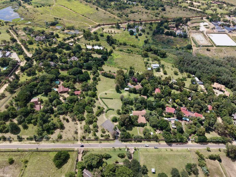 An aerial view of a residential property featuring mature landscaping, established trees, and multiple structures situated within a spacious, green environment.