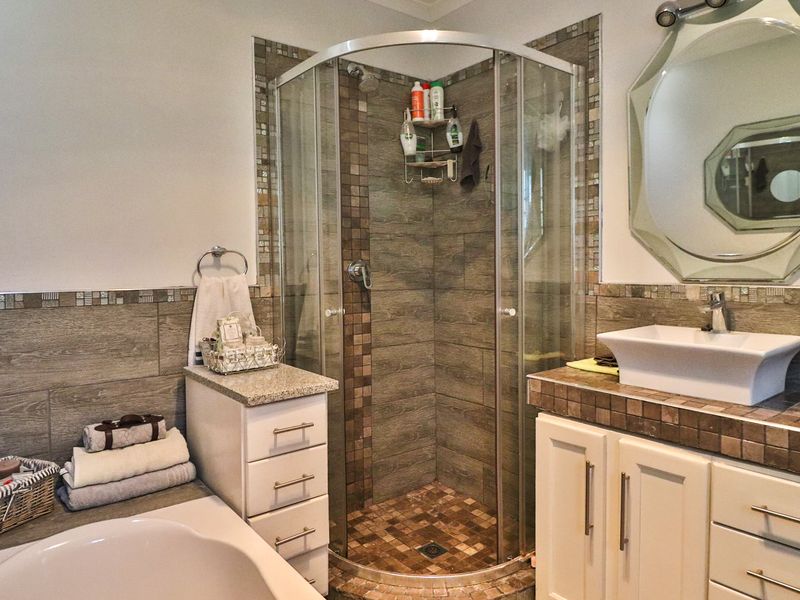 A well-appointed bathroom featuring a corner shower enclosure, vessel sink with vanity storage, and decorative tiled wall finishes.