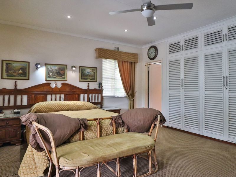 Spacious bedroom featuring built-in cupboards, carpeted flooring, and a ceiling fan, offering a comfortable and functional living space.