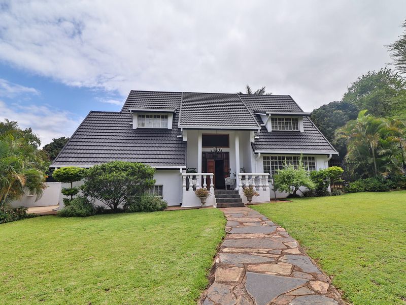 A charming double-story home featuring a dark tiled roof, stone pathway, and a welcoming covered entrance with classic balustrade detailing.