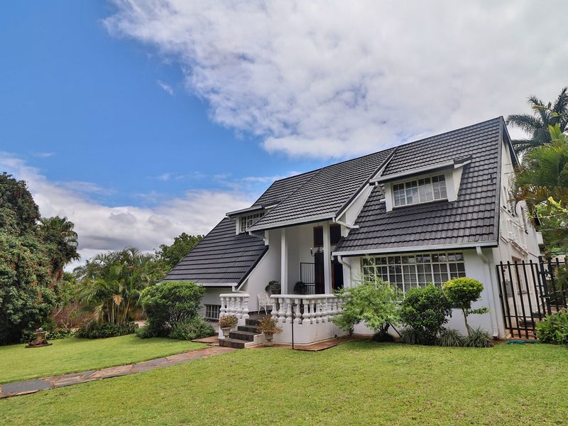 A charming double-story house featuring a dark tiled roof, white facade, and a welcoming front entrance with a decorative balustrade set in a garden.
