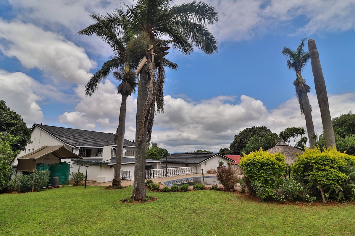 Spacious rear garden featuring a swimming pool, thatched gazebo, and water storage tanks, set against the backdrop of the main residence.