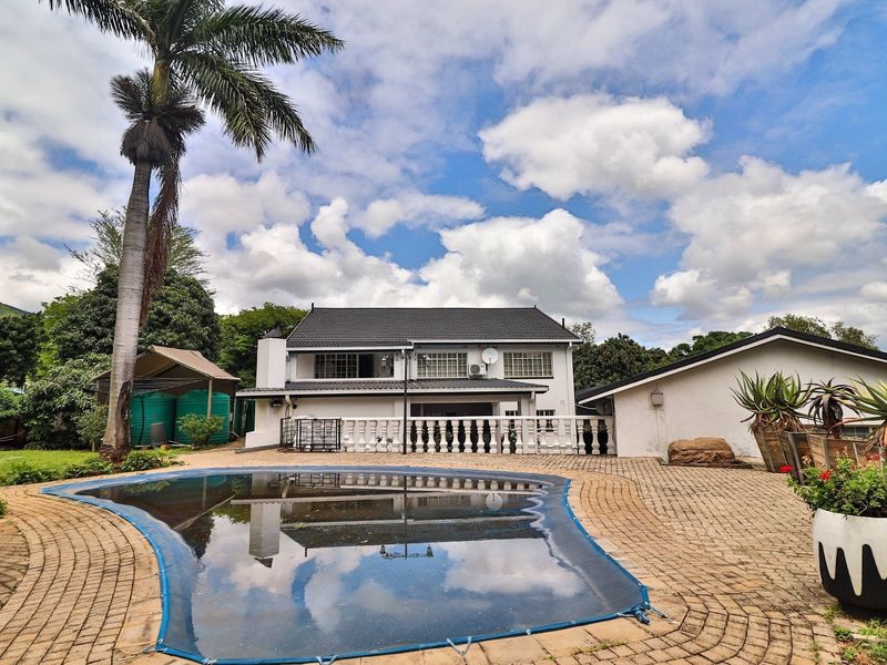 Rear exterior view featuring a swimming pool with a cover, paved patio area, and a two-story residential building with a tiled roof.