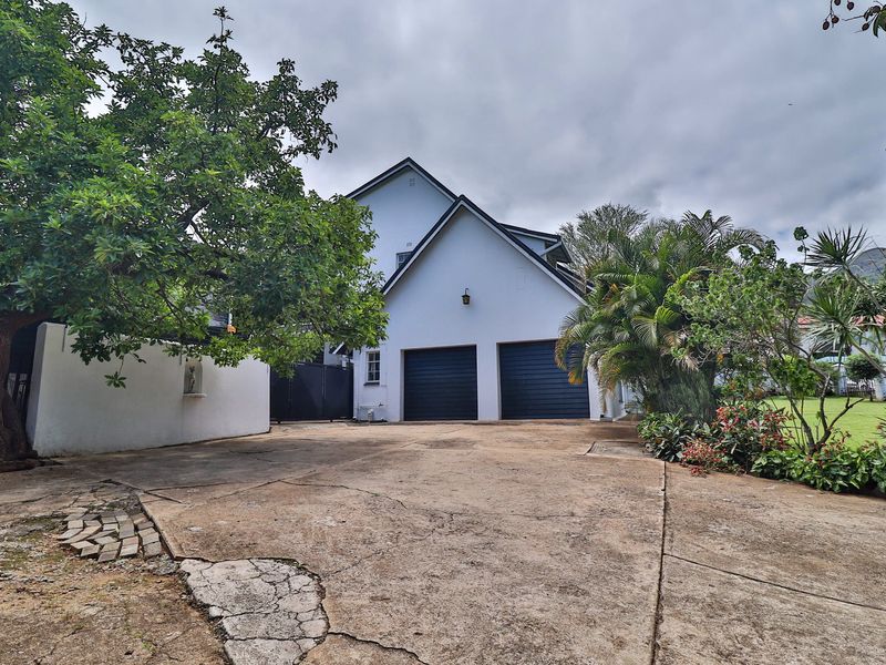 Front exterior view of the property featuring a double garage, concrete driveway, and established garden surroundings.