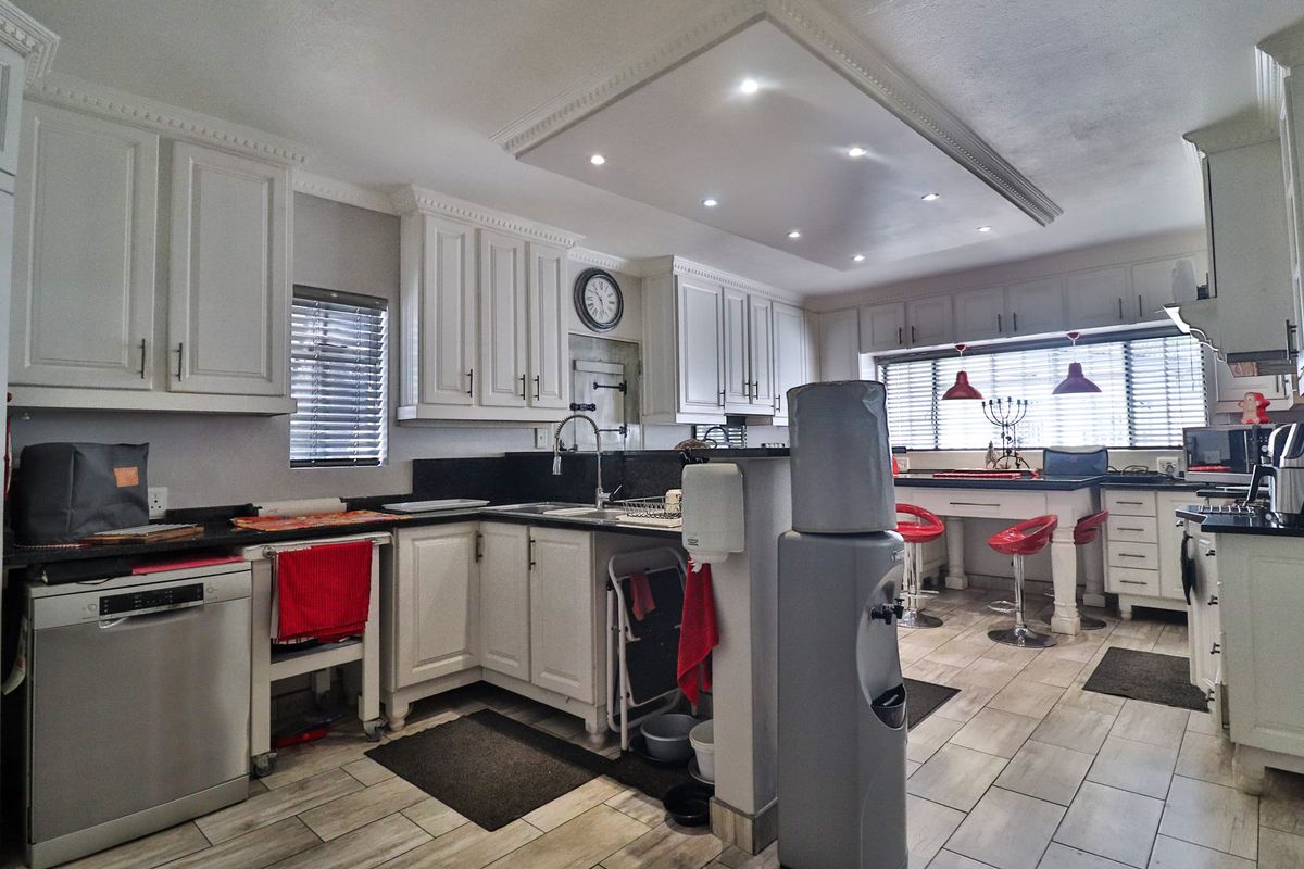 A spacious kitchen featuring white cabinetry, dark stone countertops, tiled flooring, and a central breakfast bar with recessed ceiling lighting.