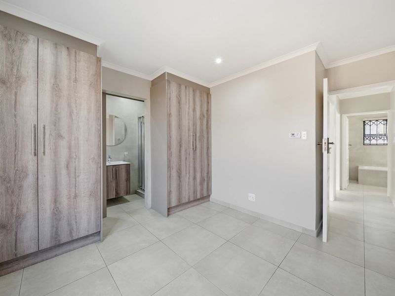 A spacious bedroom featuring neutral tiled flooring, built-in wooden cupboards, and direct access to an en-suite bathroom.