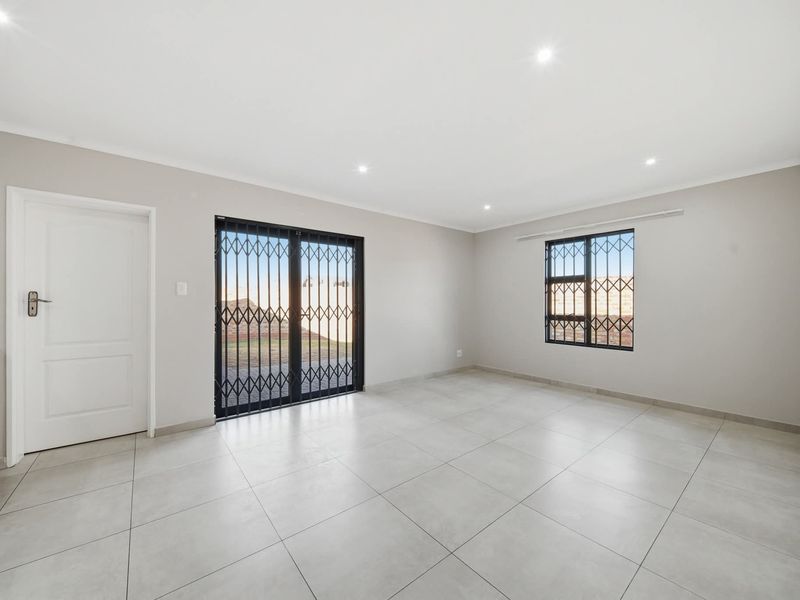 A bright, empty living room featuring neutral tiled flooring, recessed downlights, and secure access points with fitted security gates and bars.