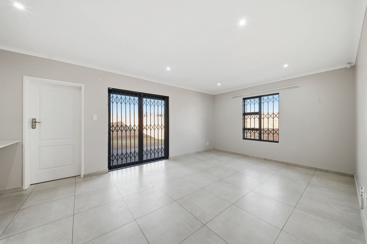 A bright, empty living room featuring neutral tiled flooring, recessed downlights, and secure access points with fitted security gates and bars.