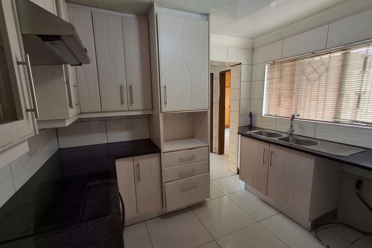 A functional kitchen featuring light-toned built-in cabinetry, dark granite countertops, a double basin sink, and tiled flooring throughout.