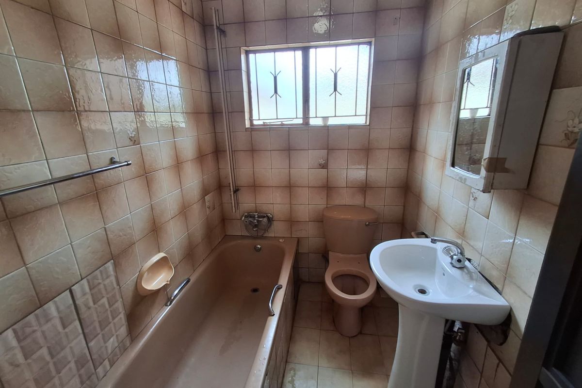 A dated bathroom featuring a bathtub, pedestal basin, and toilet with original wall tiling and security bars on the window.