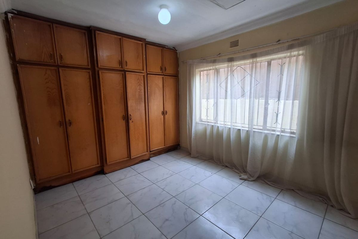A vacant bedroom featuring built-in wooden cabinetry, tiled flooring, and a window fitted with security bars.