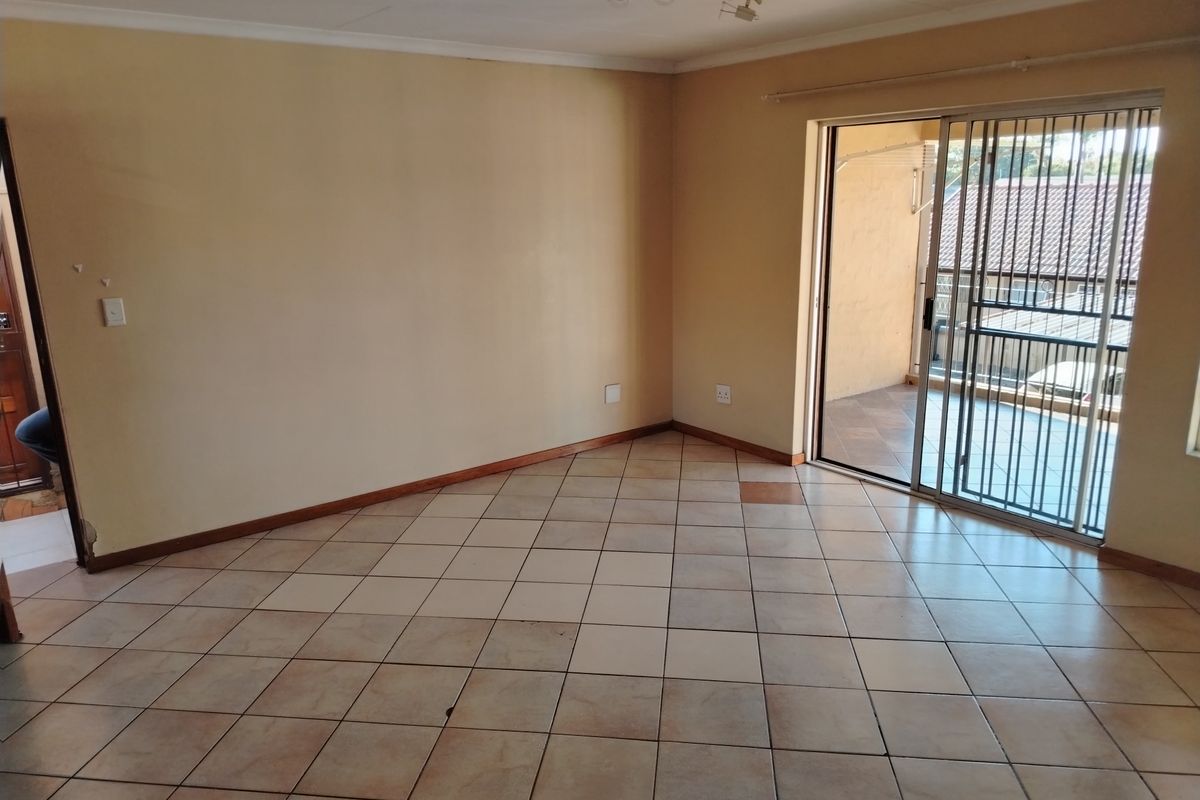 An empty living room featuring tiled flooring, a ceiling-mounted light fixture, and a sliding glass door providing access to an outdoor balcony area.
