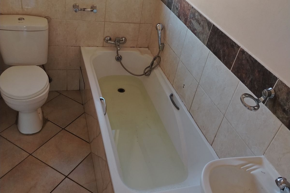 A functional bathroom featuring a bathtub with shower attachment, a pedestal basin, and a toilet, finished with neutral wall and floor tiling.