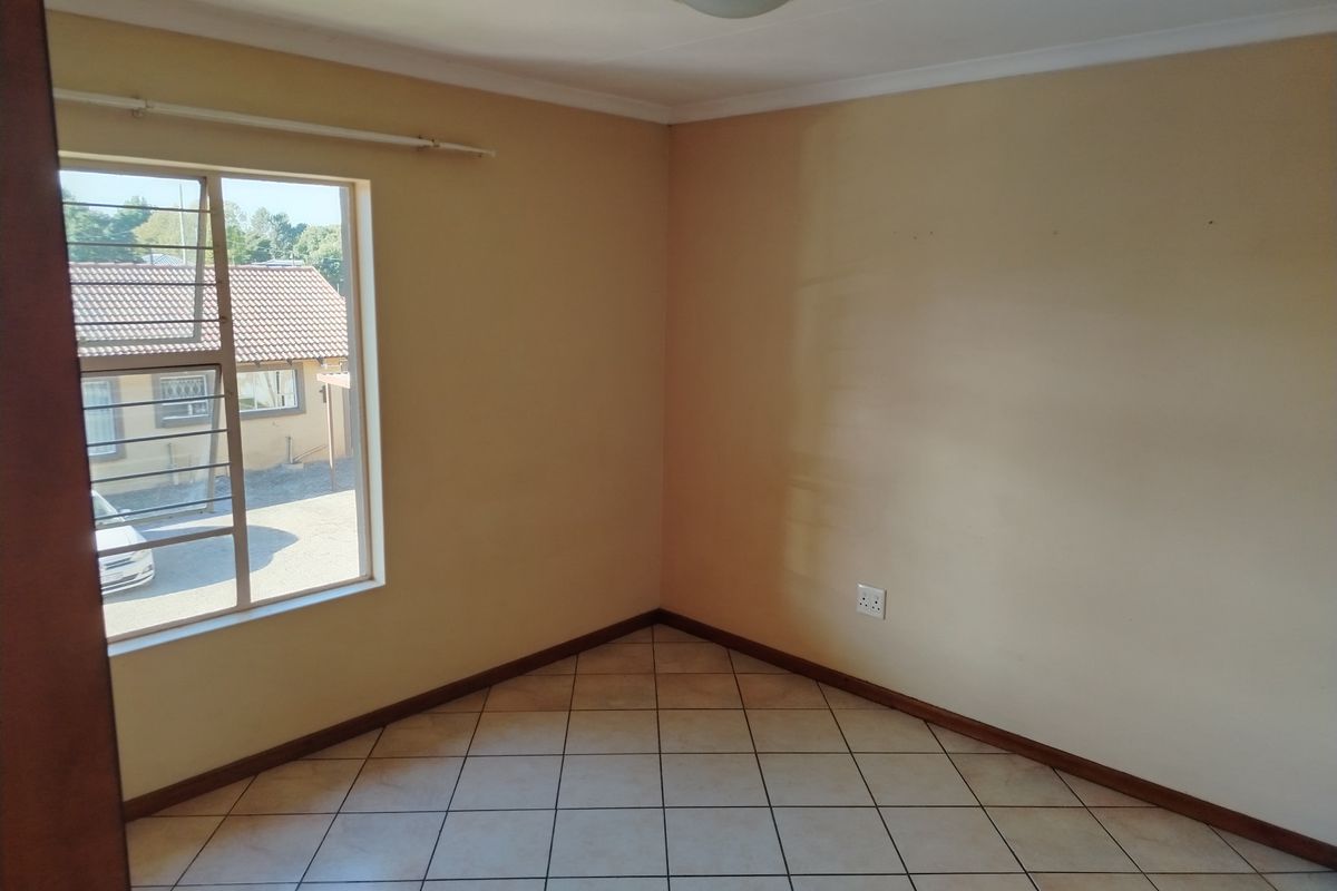 A vacant bedroom featuring neutral wall paint, tiled flooring, and a window with security bars.