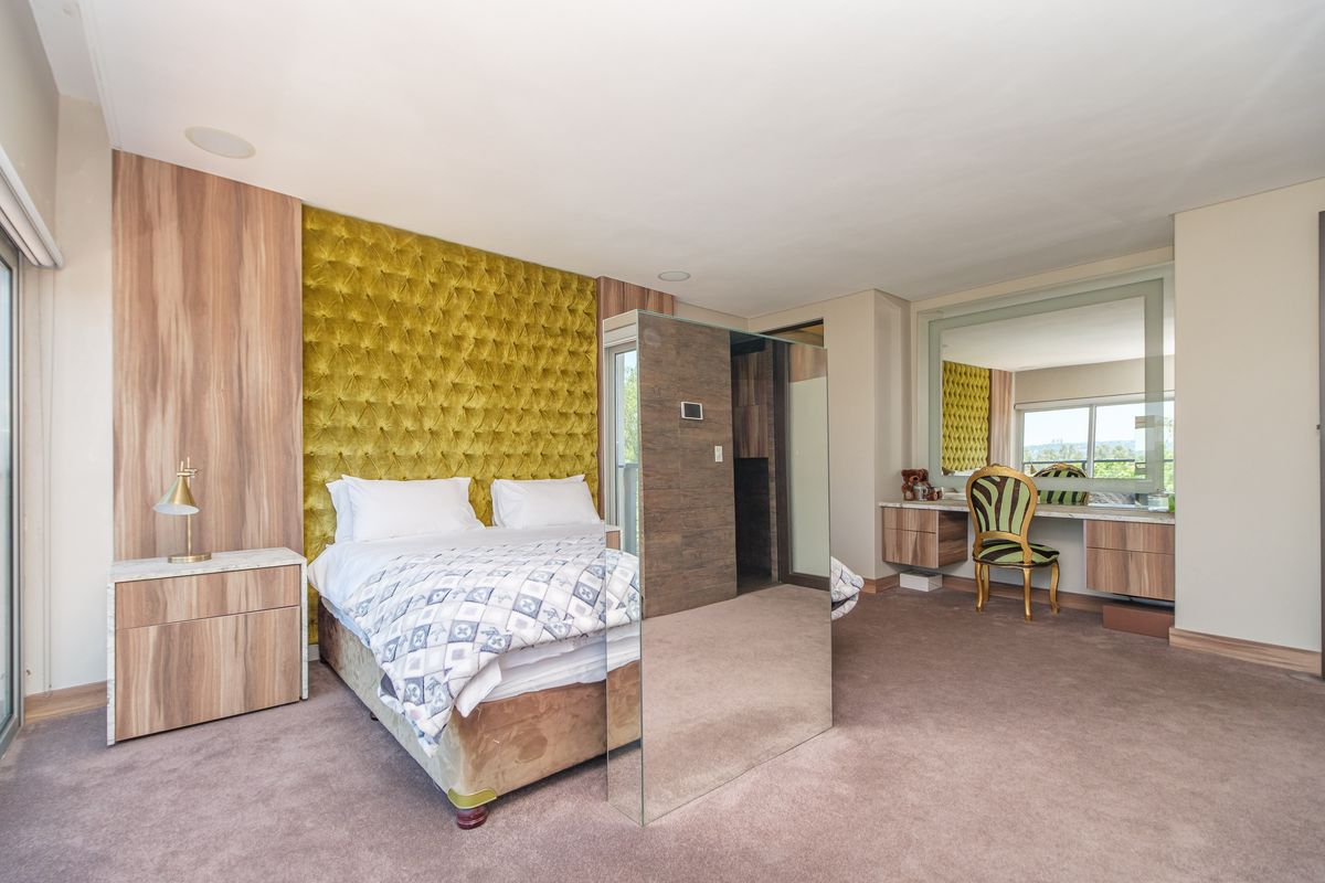 Spacious bedroom featuring a built-in headboard, integrated vanity area with mirror, and neutral carpeting, offering a modern and comfortable living space.