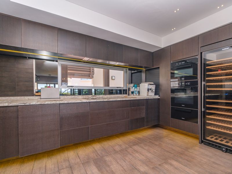 Modern kitchen featuring dark wood cabinetry, stone countertops, integrated Miele ovens, and a built-in wine cooler with recessed under-cabinet lighting.