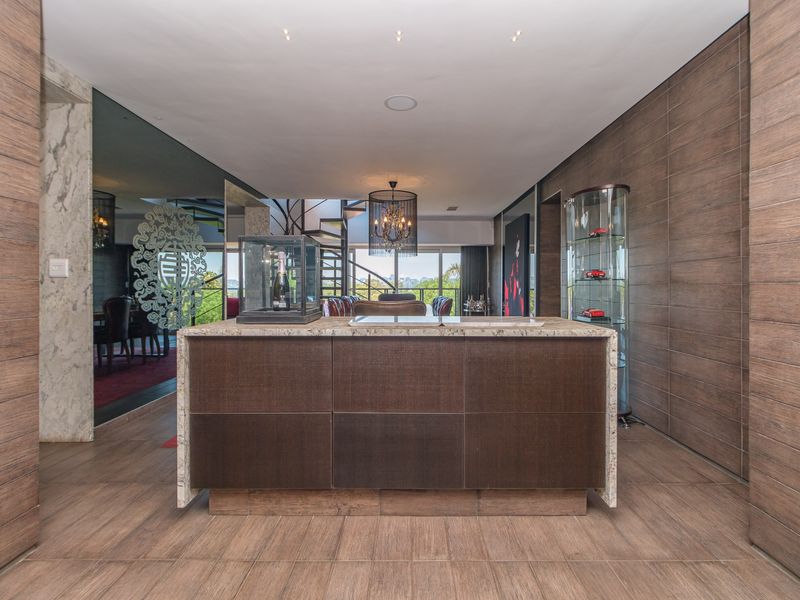 A sophisticated open-plan living area featuring a central stone-topped island, wood-paneled walls, recessed lighting, and a striking spiral staircase leading to the upper level.