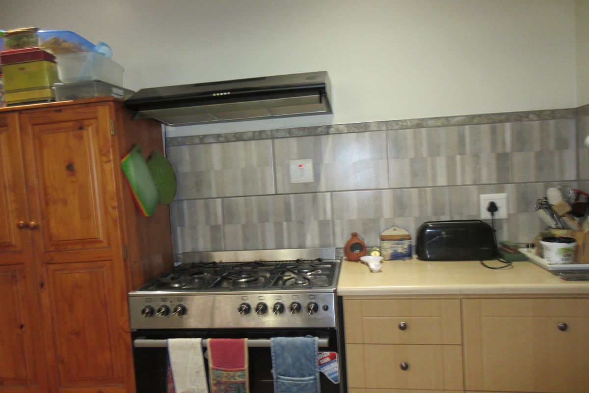 A functional kitchen area featuring a gas stove, extractor fan, tiled backsplash, and built-in cabinetry with laminate countertops.