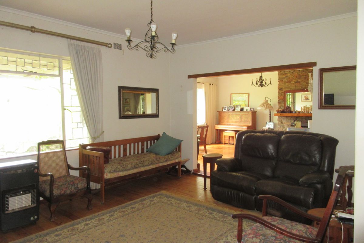 Spacious living room featuring hardwood flooring, a stone fireplace, and natural light, offering a comfortable and traditional living space.