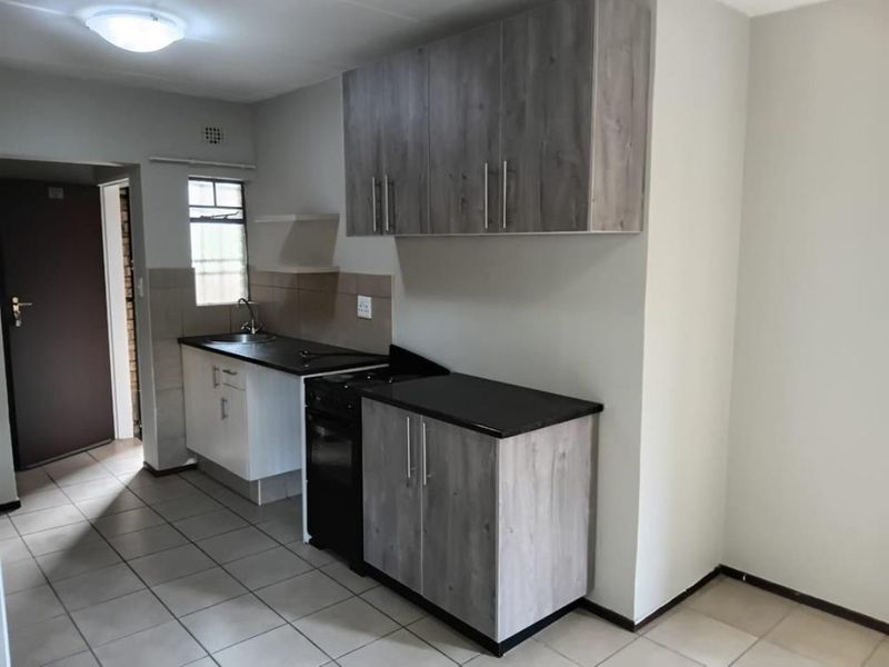 A functional kitchen featuring wood-look cabinetry, dark countertops, a stainless steel sink, and a freestanding stove with tiled flooring.
