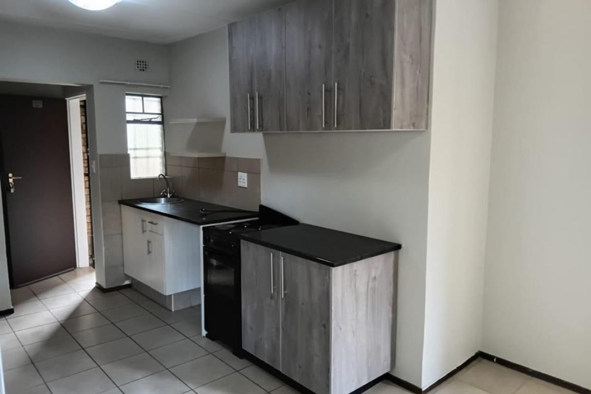 A functional kitchen featuring wood-look cabinetry, dark countertops, a stainless steel sink, and a freestanding stove with tiled flooring.