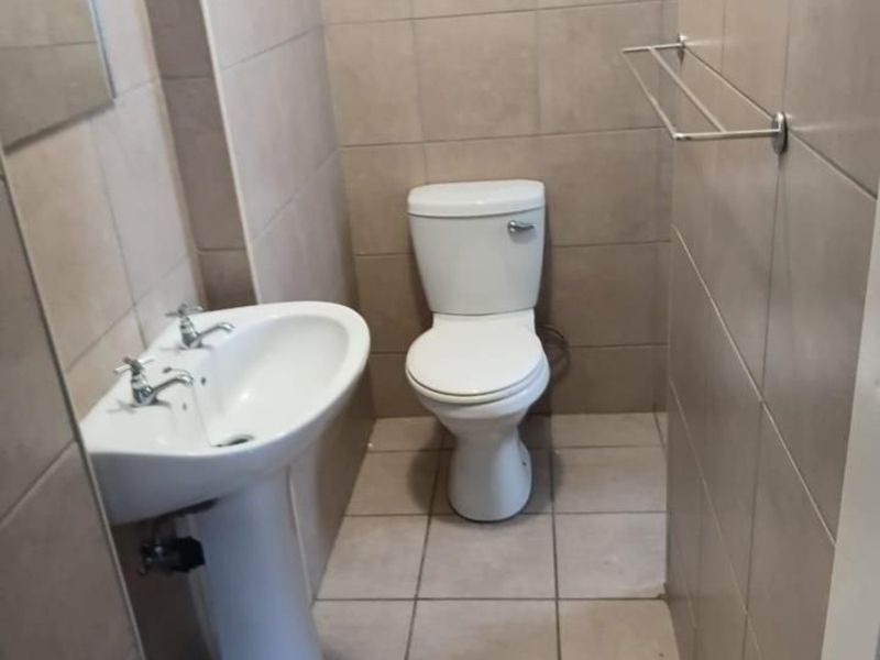 A compact bathroom featuring a pedestal basin, toilet, and neutral floor-to-ceiling wall tiling.