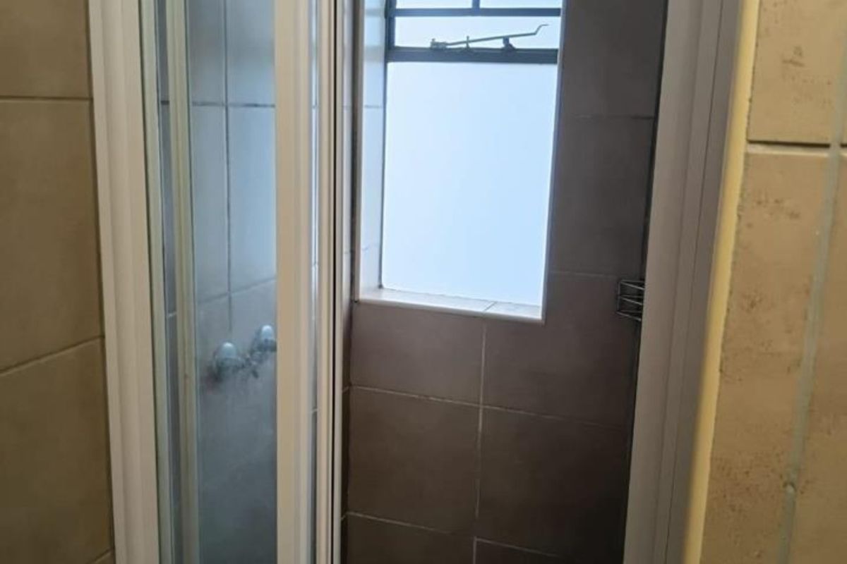 A functional bathroom shower area featuring tiled walls, a glass shower enclosure, and a small window for natural light and ventilation.