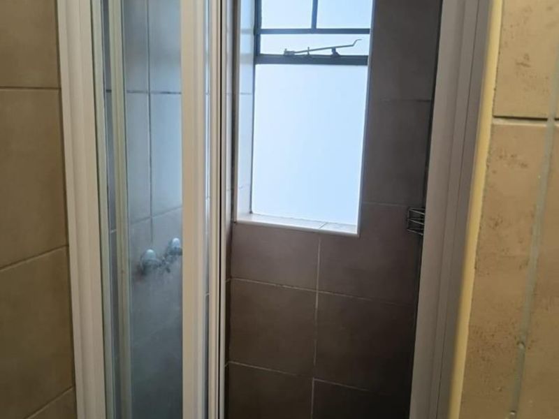 A functional bathroom shower area featuring tiled walls, a glass shower enclosure, and a small window for natural light and ventilation.