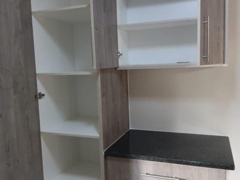 A clean, modern scullery or pantry area featuring built-in wood-look cabinetry and a dark laminate countertop, providing ample storage space.