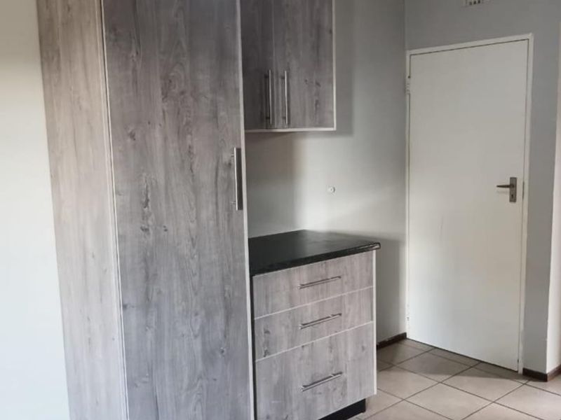A compact kitchen area featuring modern grey wood-look cabinetry, a dark laminate countertop, and neutral tiled flooring.
