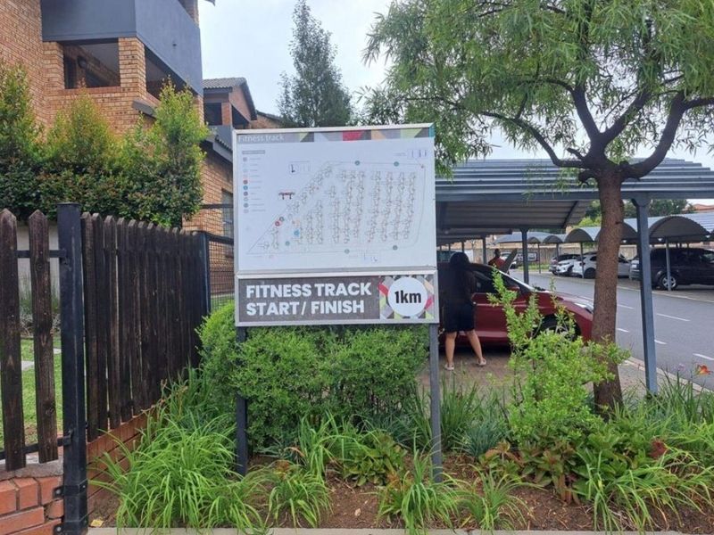 Exterior view of the apartment complex grounds featuring a fitness track signage, covered parking bays, and landscaped garden areas.