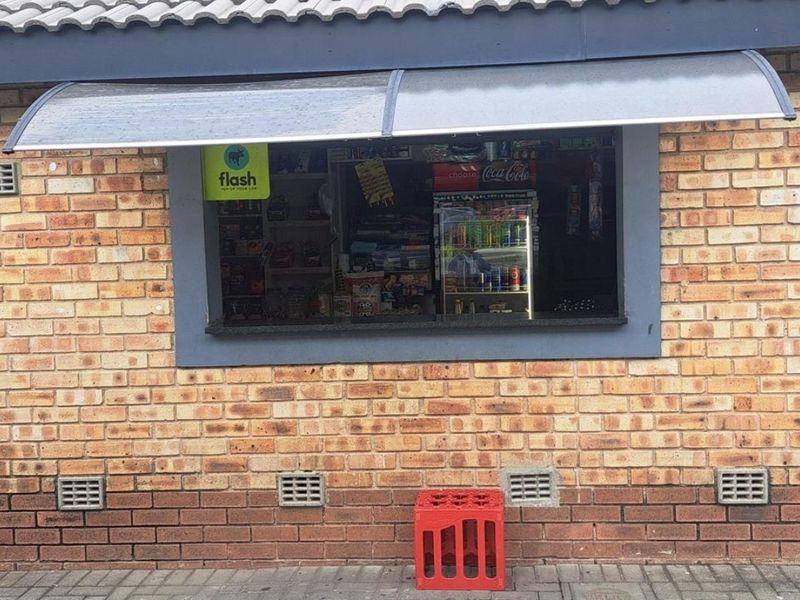 Exterior view of a commercial service window set into a face brick wall, featuring a protective polycarbonate awning and integrated ventilation vents.
