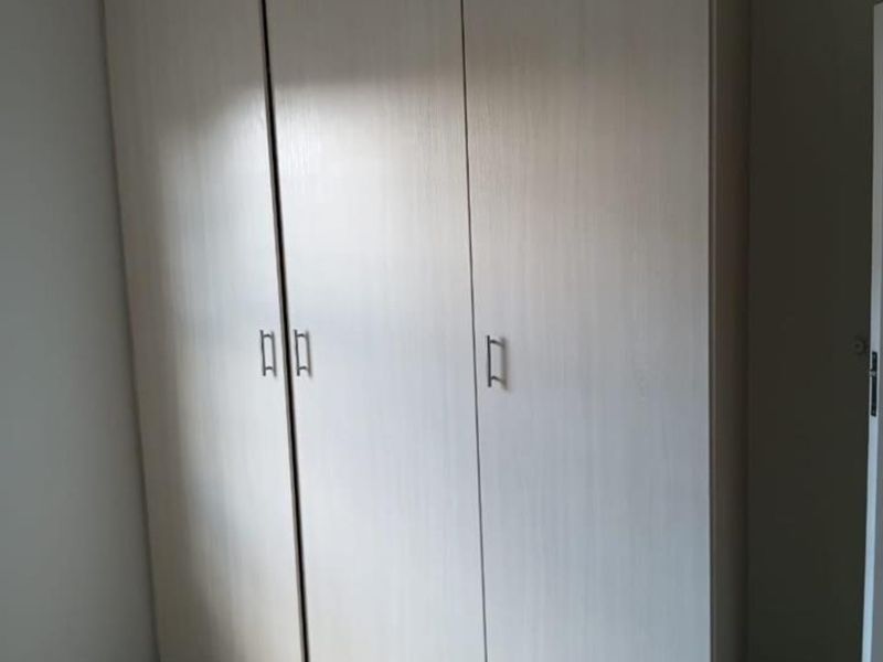 A clean bedroom interior featuring a neutral-toned built-in wardrobe and tiled flooring, offering a functional and well-maintained storage solution.