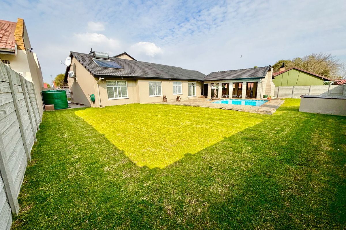 Rear view of the property featuring a landscaped garden, swimming pool, and a covered patio area with tiled roofing.